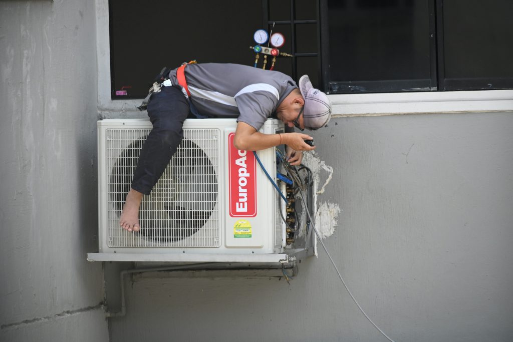 A technician skillfully repairing an outdoor air conditioning unit mounted on a building wall.